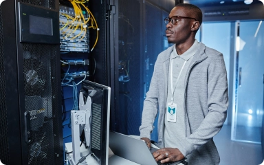 Young man diagnosing server with a laptop in the server room
